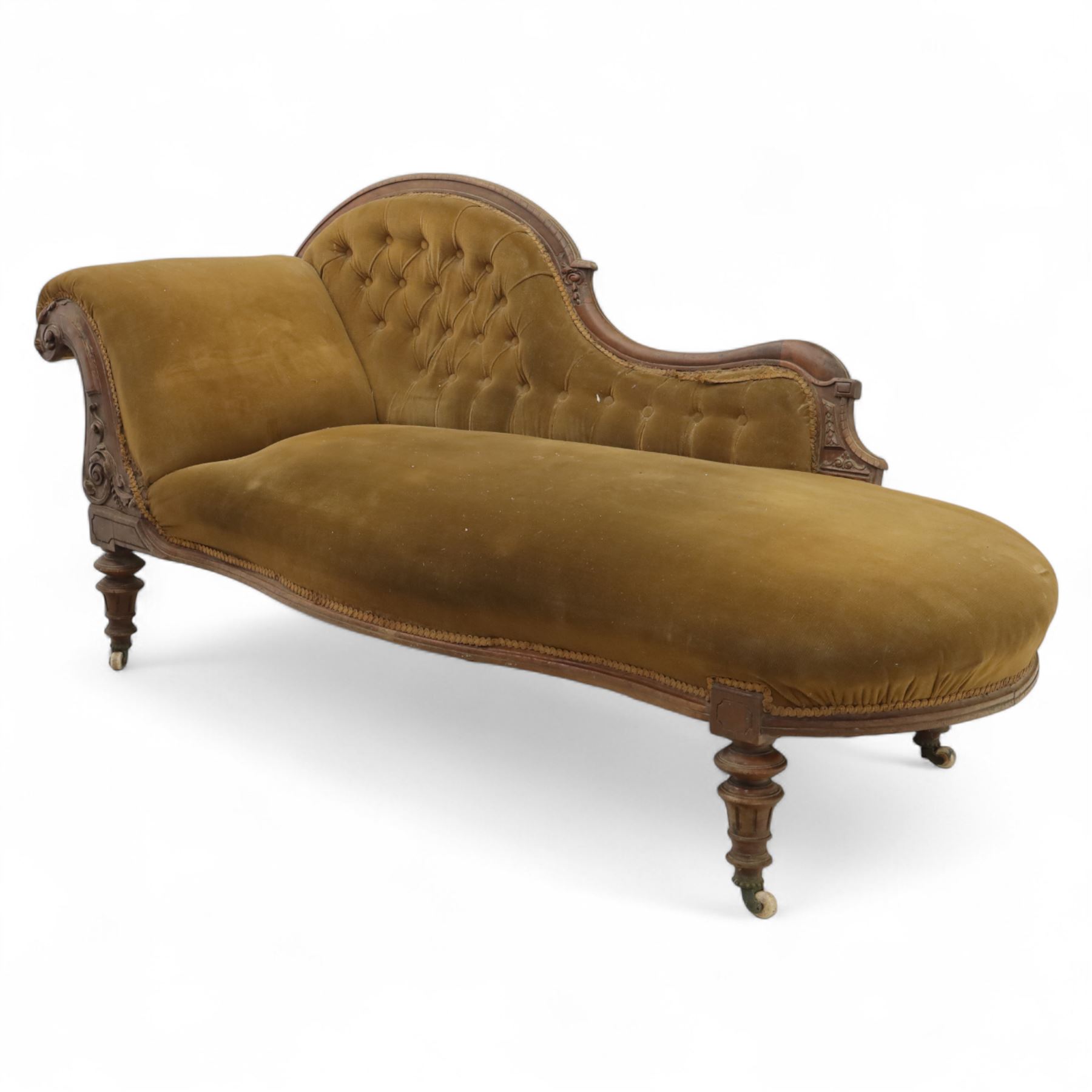 Victorian walnut framed Chaise longue, with carved scroll decoration and an out-swept buttoned upholstered, padded back and scroll end, seat upholstered mustard coloured velvet fabric, raised on turned legs with ceramic castors 