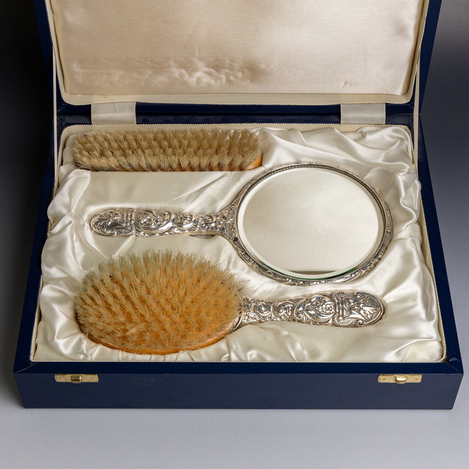 Silver mounted three piece dressing table set, comprising hand mirror, hairbrush and clothes brush, all with embossed green man and floral decoration, stamped Filled and hallmarked Broadway & Co, Birmingham 2001, contained within presentation box