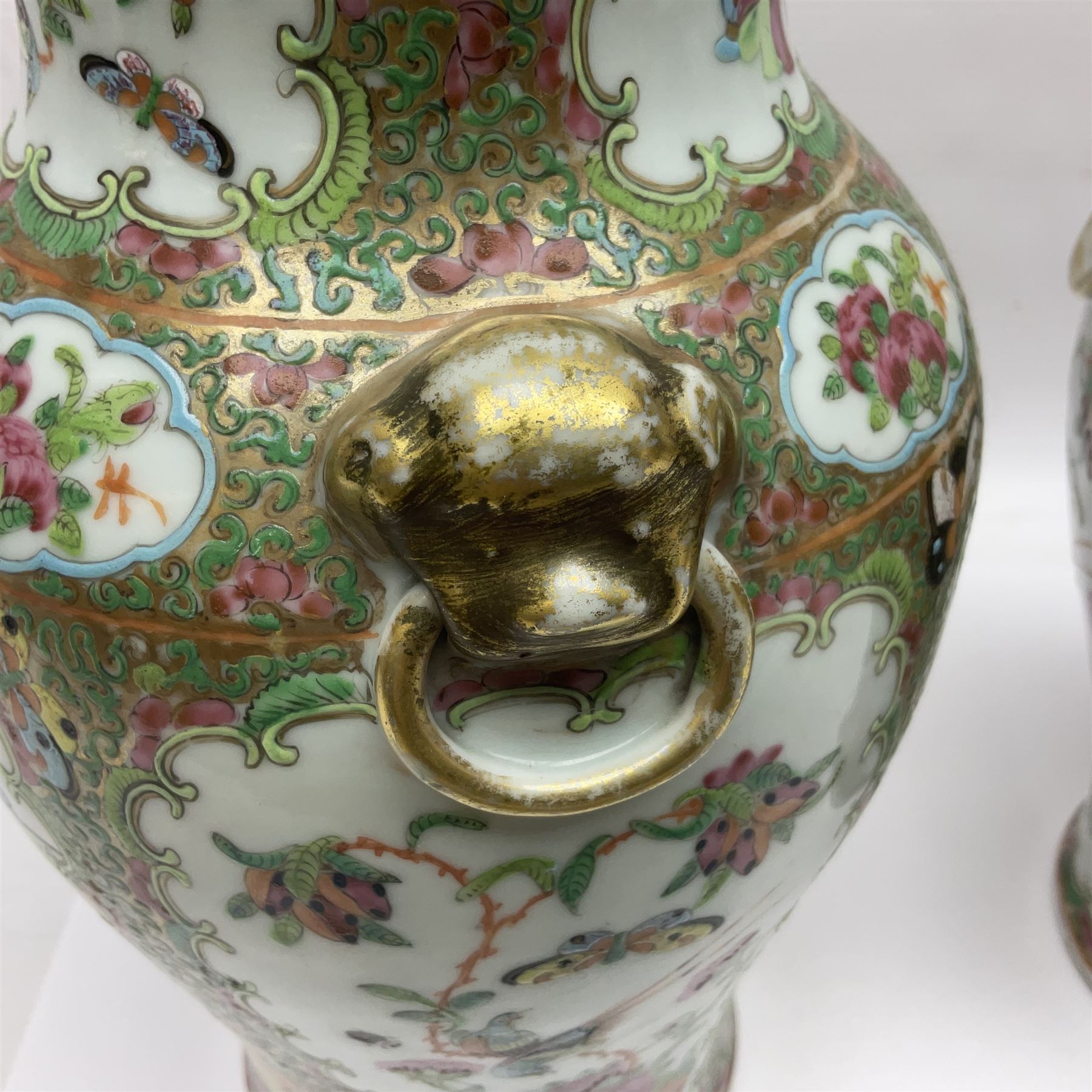 Pair of 19th century Chinese Famille Rose vases and covers, each of baluster form with twin gilt lion mask ring handles to shoulders, the flattened domed covers with gilt temple lion finials, each decorated with alternating reserves of bijin and attendants, and birds and butterflies amongst blossoming peonies, against a gilt ground profusely decorated with stylised scrolls, H32.5cm