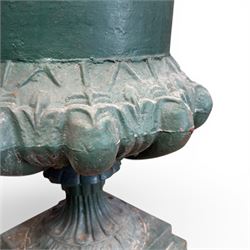 Pair of Victorian cast iron campana garden urns, the flared rim with repeating stylised anthemion motifs with scrollwork, over a deep gadrooned and Aesthetic moulded underbelly, fluted and foliate lower bowls on square pedestal bases, in antique green-painted finish