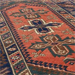 Caucasian Kazak rug, red field with three bold geometric medallions in dark blue, cream and brown, scattered tribal motifs, broad indigo border decorated with stylised hooked forms and multiple narrow patterned borders