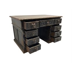 Late 19th century Gothic revival carved oak twin pedestal desk, rectangular top with inset writing surface and carved edges, central frieze drawer flanked by eight drawers, all with green man carved handles and extending trailing foliage, carvings of pineapple and lion mask corbels, the pedestals with panelled sides and back, on plinth bases