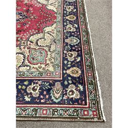 Large Persian carpet, the red ground field decorated with large rosette medallion, trailing foliate design decorated with stylised plant motifs, pale ground spandrels decorated with scrolls, repeating stylised flower head border with guards 