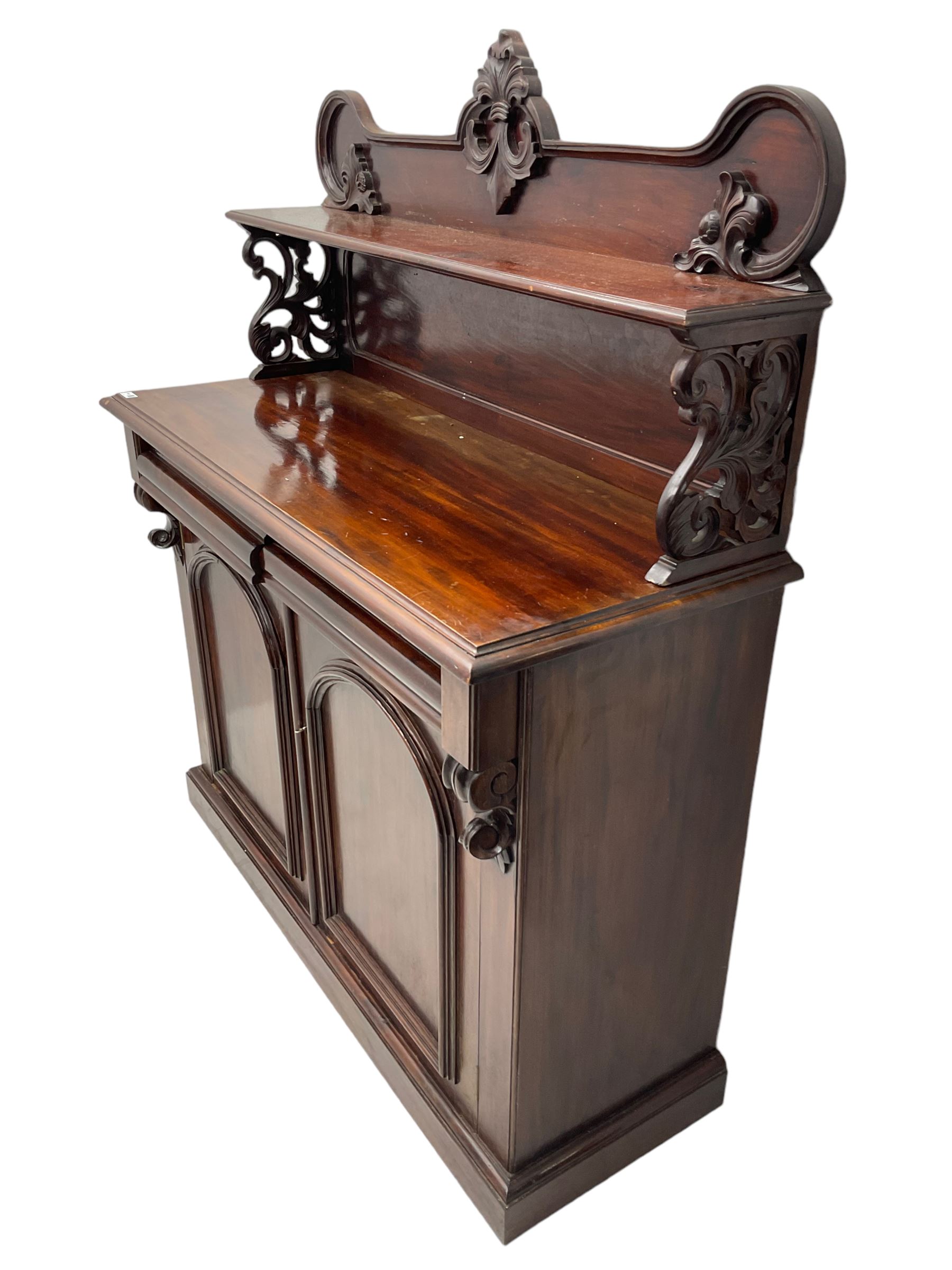 Victorian mahogany chiffonier, raised shaped back with foliage scroll carved mounts, on fretwork and carved bracket supports, moulded rectangular top over two frieze drawers and double panelled cupboard, on moulded plinth base