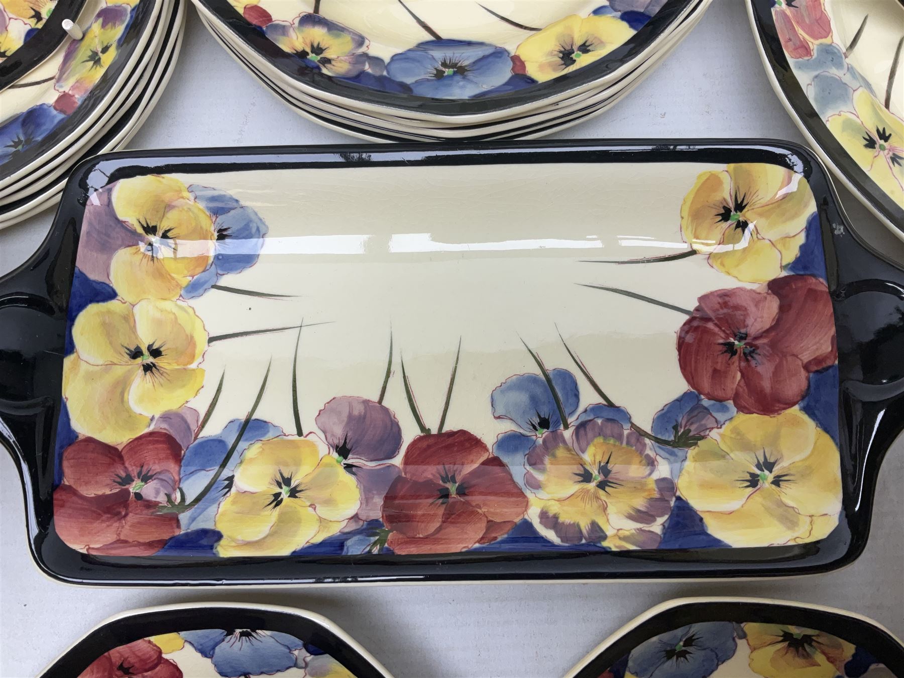 Early 20th century Art Deco Royal Doulton Pansies pattern octagonal teawares, comprising three larger teacups and saucers, three smaller teacups and saucers, open sucrier, two jugs, slop bowl, six side plates, two larger plates, two small circular dishes and one long twin handled rectangular dish, all with printed marks beneath, Rd No 597783, pattern no D4049