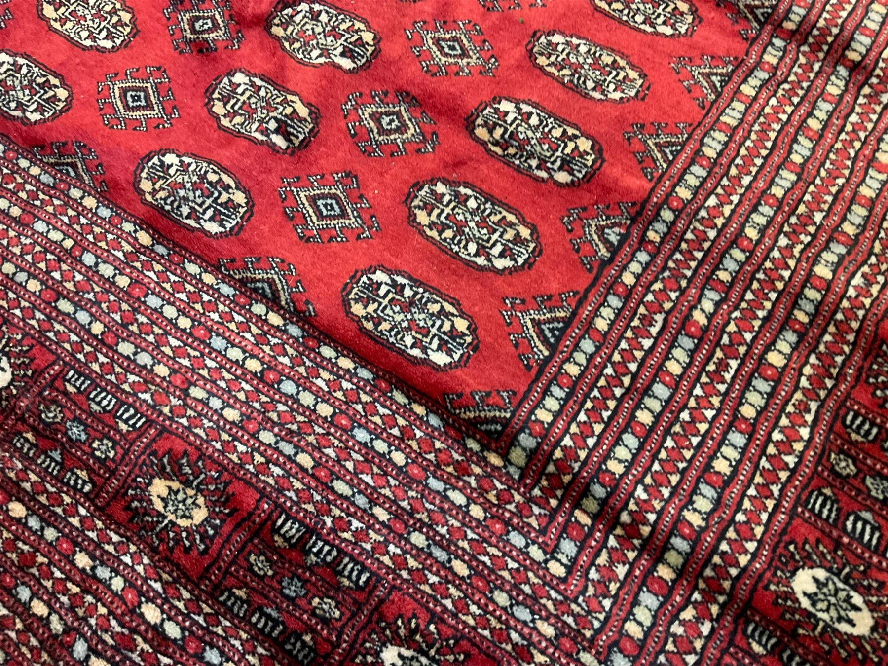Persian Bokhara crimson ground carpet, the field decorated with repeating Gul motifs and lozenges, the multi-band geometric border with stylised plant motifs, two additional bands at the ends with geometric lozenges