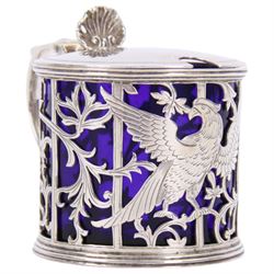 Early 20th century silver mustard pot and cover, of drum form the sides pierced with hound and birds in flight against leafy vines, the plain flat topped hinged cover with shell thumb piece opening to reveal a removable blue glass liner, hallmarked Joseph Rodgers & Sons, Sheffield 1929, including thumb piece H7cm