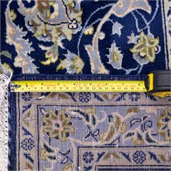 Central Persian Kashan hand-knotted rug, deep blue all-over field, finely decorated with dense scrolling floral sprays, palmettes, and flowering vines in ivory, soft gold, and pale green tones, enclosed by a multi-band floral border with corresponding guard stripes, with cotton fringe ends, signed Shah Abassi Workshop 