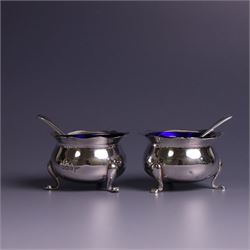 Early 20th Century four piece silver cruet set, comprising a pair of pepper shakers and a pair of open salts, each of circular form with shaped rims and upon three pad feet, hallmarked Walker & Hall, Sheffield 1912, the open salts with two silver plated salt spoons and blue glass liners 