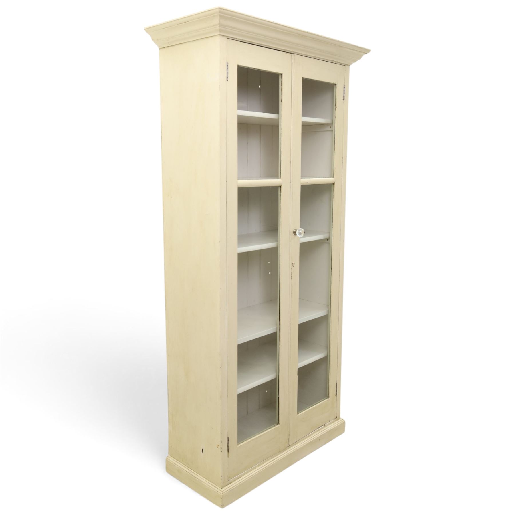 Traditional white painted pine display cabinet, projecting cornice above two glazed doors enclosing five fixed shelves, tongue and groove back raised on a plinth base