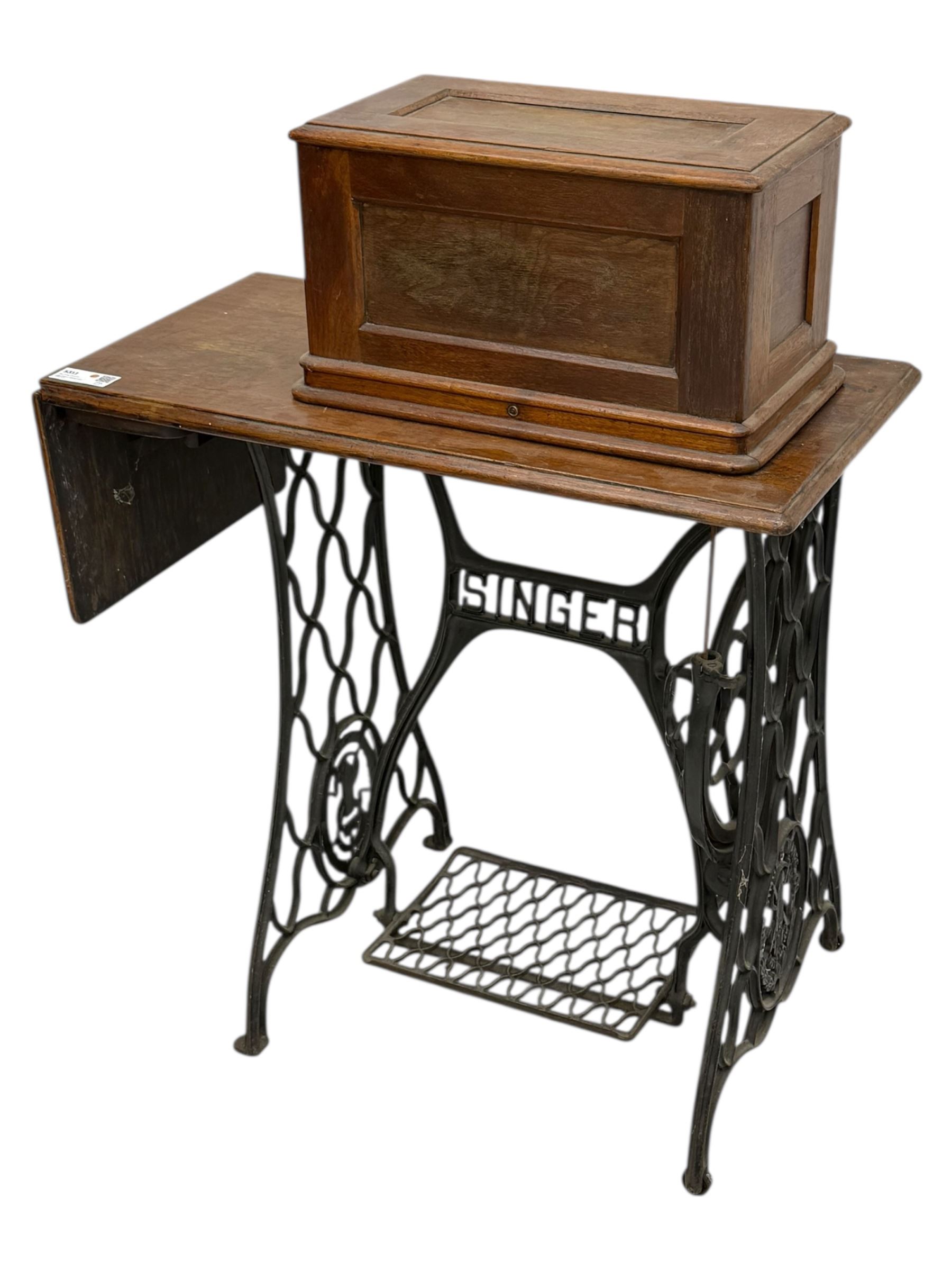 Singer - early 20th century cast iron treadle sewing machine, with hand crank wheel and oak work surface, the machine decorated with gilt foliate detail, complete with rectangular wooden cover and folding extension leaf