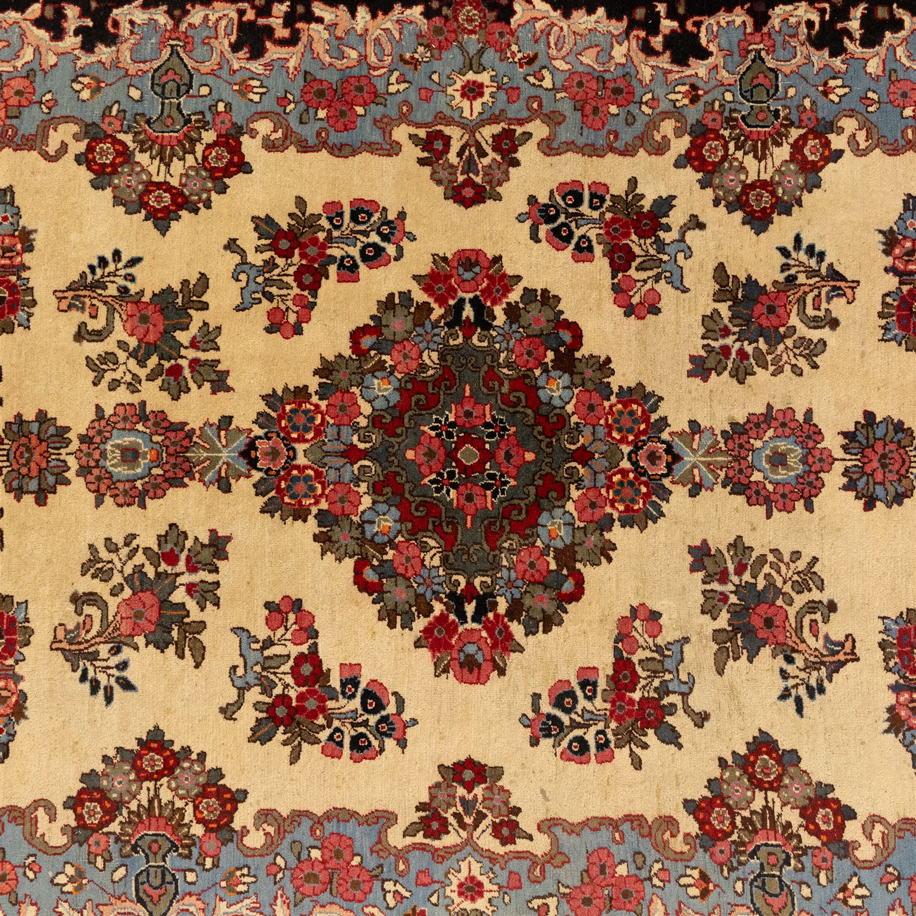 Central Persian Kashan hand-knotted carpet, cream ground, with a central lobbed floral burgundy, rose, and indigo medallion, surrounded by scrolling sprays of carnations and palmettes, with sky blue spandrels decorated with curvilinear vines and stylized blossoms, framed by a repeating terracotta border of palmettes, framed by narrow guard stripes 