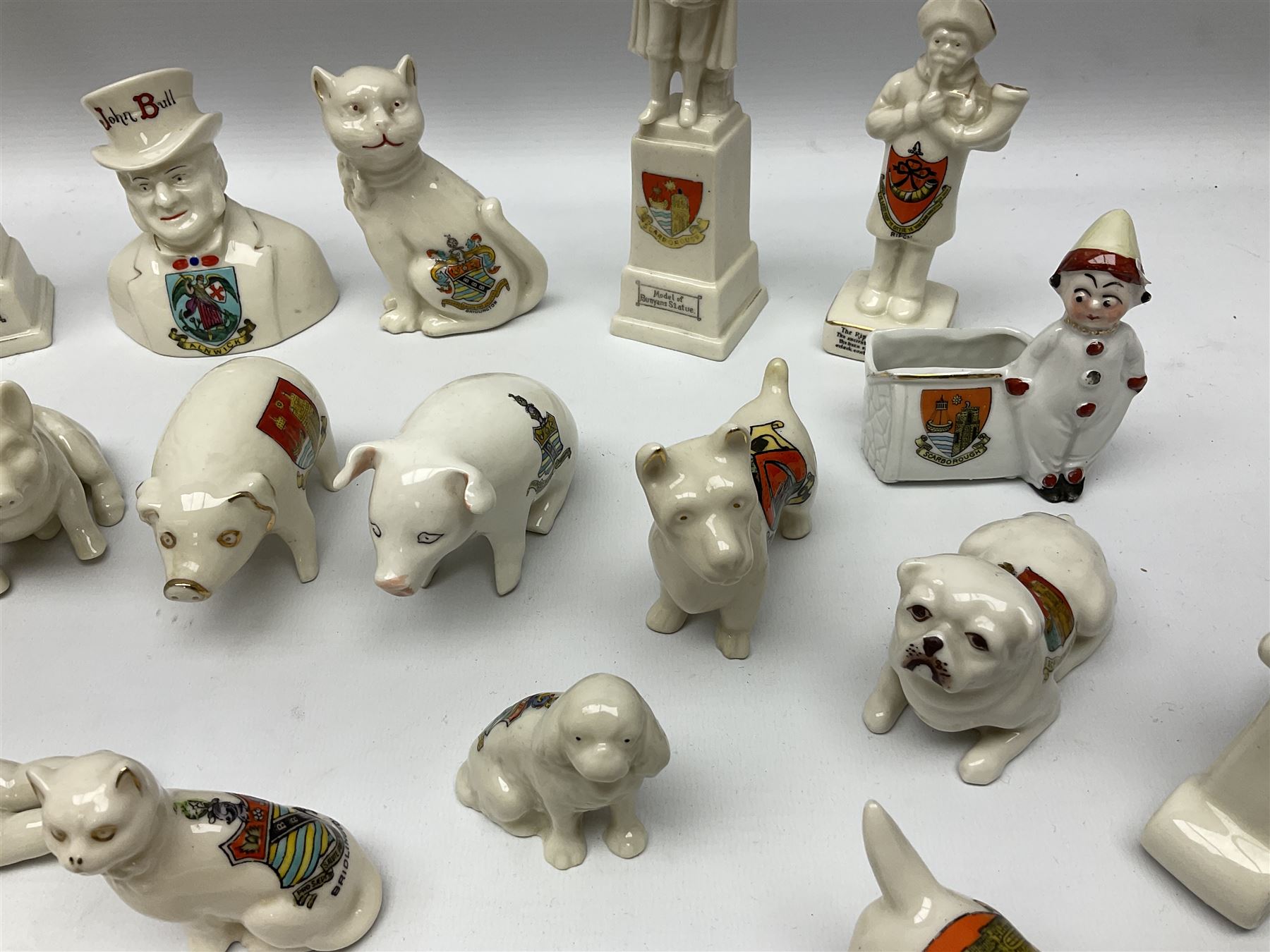 Collection of figural crested ware, to include Carlton Chins John Bull Alnwick, Clifton China Cheshire Cat,  Arcadia pig, Crafton crawling baby and another seated baby, quantity of cat, dog and pig figures, two Willow Art Model of Bunyans Statue, Toby jug, Victoria China, Arcadan bulldog, fish etc