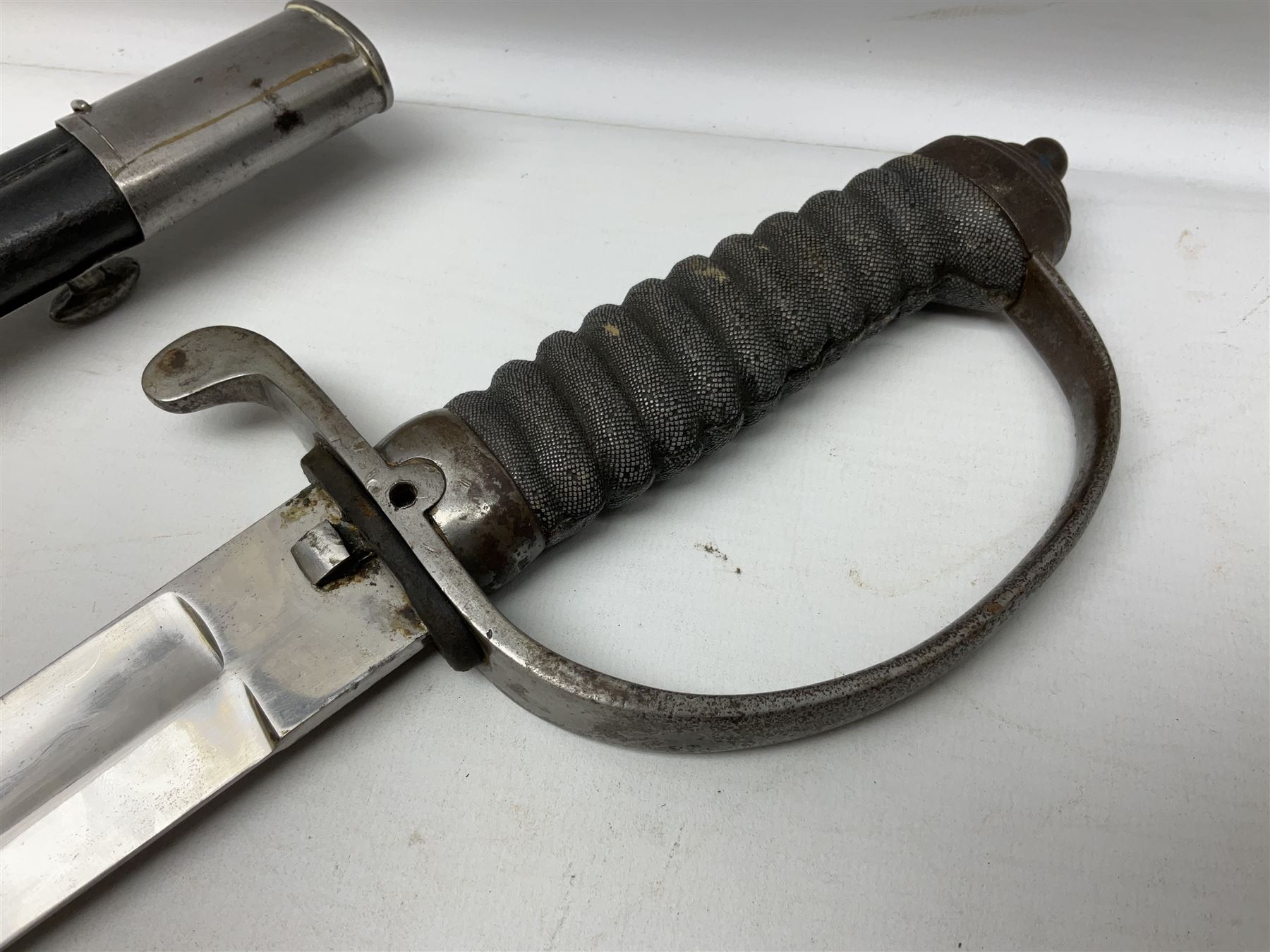 Mid-19th century Custom’s officer/Constabulary sidearm, with plain 60.5cm slightly curving fullered blade double edged at tip,  steel knucklebow and downswept quillon, stepped pommel and ribbed fishskin grip; in leather covered scabbard with steel locket, frog stud and chape L76cm overall