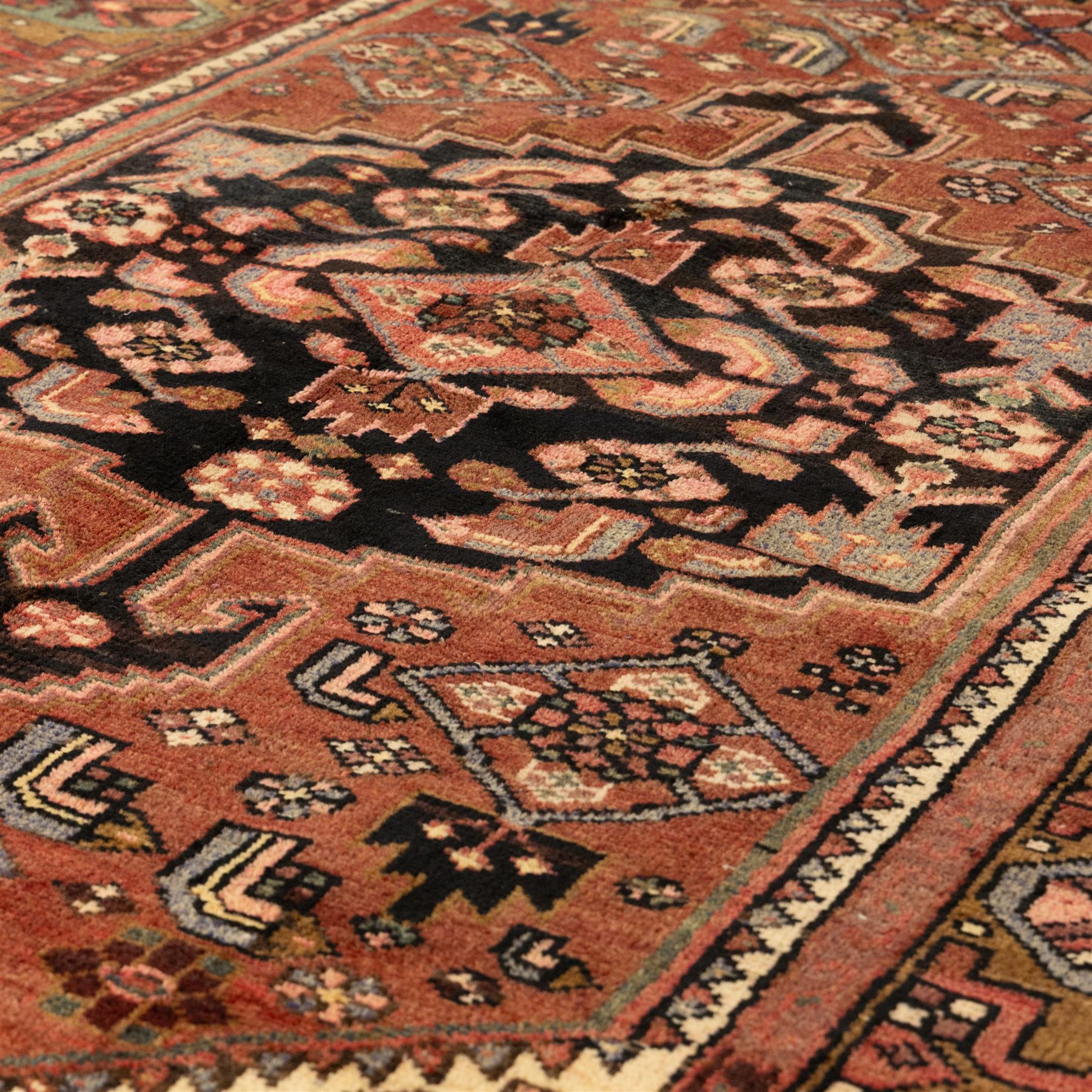 North West Persian Zanjan hand-knotted rug, madder-red field with a central stepped lozenge medallion enclosing stylized geometric floral motifs in indigo, ivory, and brown, angular spandrels filled with tribal devices and framed by a series of geometric borders with latch-hook rosette and leaf motifs, with cotton fringe ends  