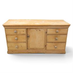 Victorian stripped pine sideboard, rectangular plank top rounded edges, with central cupboard door with shaped panel, flanked by two banks of three graduating drawers with turned knobs, raised on a plinth base 