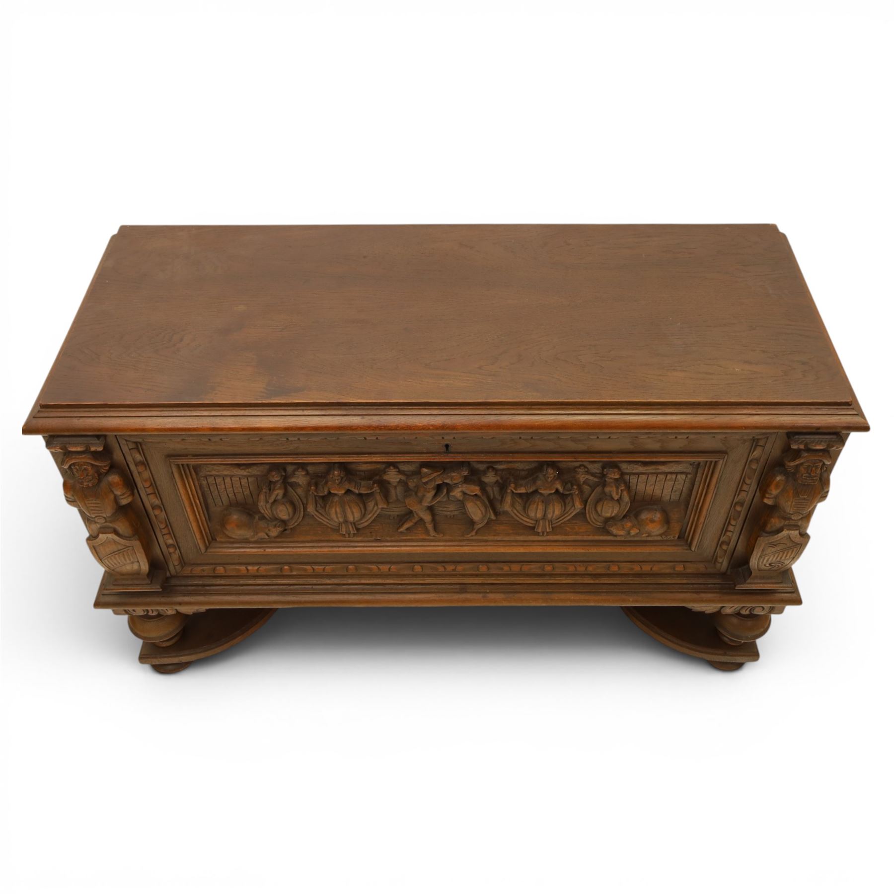 Carved oak coffer bench, rectangular moulded top above carved fall front, with figural, mask and foliate decoration, panelled sides, raised on turned bun feet with shaped lower apron
