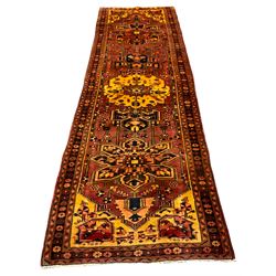 Persian Heriz golden red ground runner, then main field decorated with three stylised medallions and various motifs, three band border decorated with flower heads 