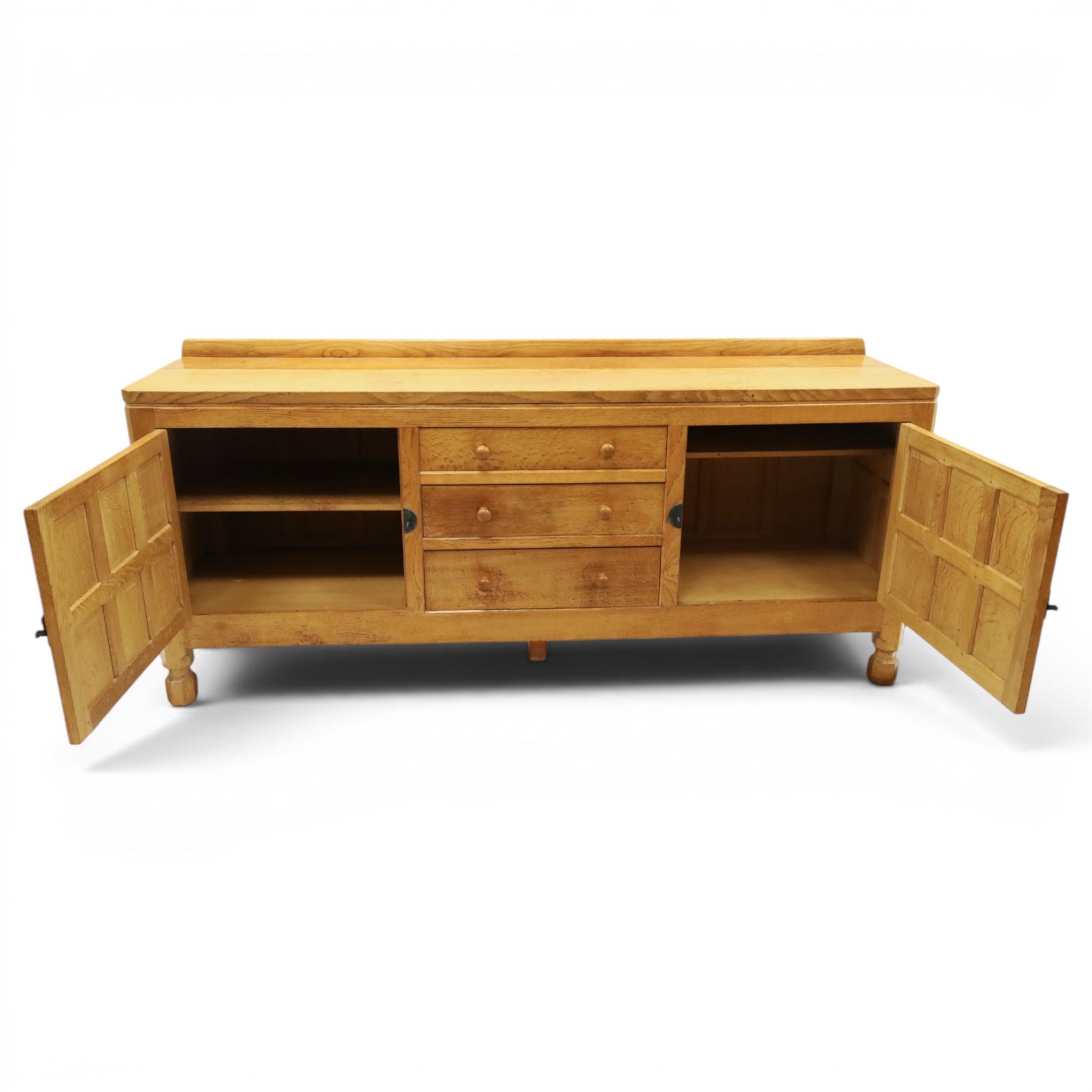 Mouseman - large adzed light oak sideboard, the rectangular top with raised galleried back, fitted with three central drawers flanked by panelled cupboards enclosing shelves, with wrought iron fittings, raised on octagonal feet, with signature carved mouse, by the workshop of Robert Thompson, Kilburn