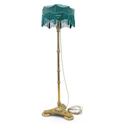 Art Deco brass standard lamp, telescopic column with level action, ring turned collars, raised on a shaped tri-form base with fluted pad feet, complete with green fabric fringed shade