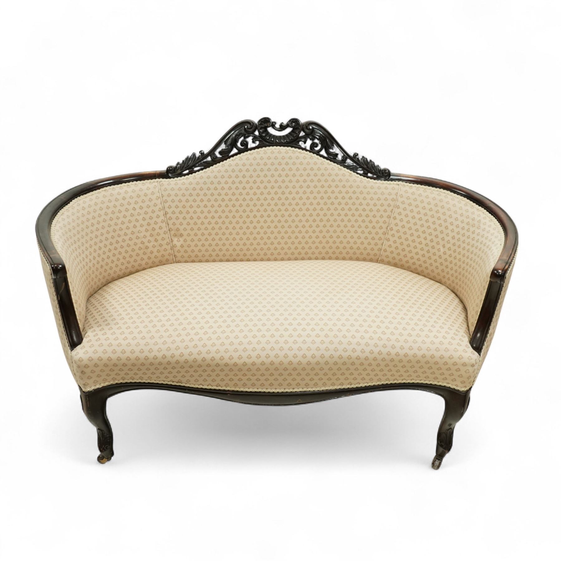 Victorian mahogany upholstered settee, the shaped back with pierced foliate carved cresting, upholstered in cream patterned fabric with serpentine seat, on cabriole front legs with brass castors