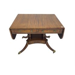 Regency period mahogany drop-leaf sofa table, rectangular top fitted with two cockbeaded drawers with ebony stringing, raised on turned columns united by quadrupod base, the sabre supports terminating in brass cups and castors