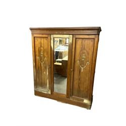 Late 19th century Arts and Crafts pitch pine triple wardrobe, shaped projecting cornice, central door with rectangular mirror plate, flanked by two panelled doors with floral foliate painted designs with trailing garlands, raised on plinth base, interior fitted with four sliding open shelves over four drawers