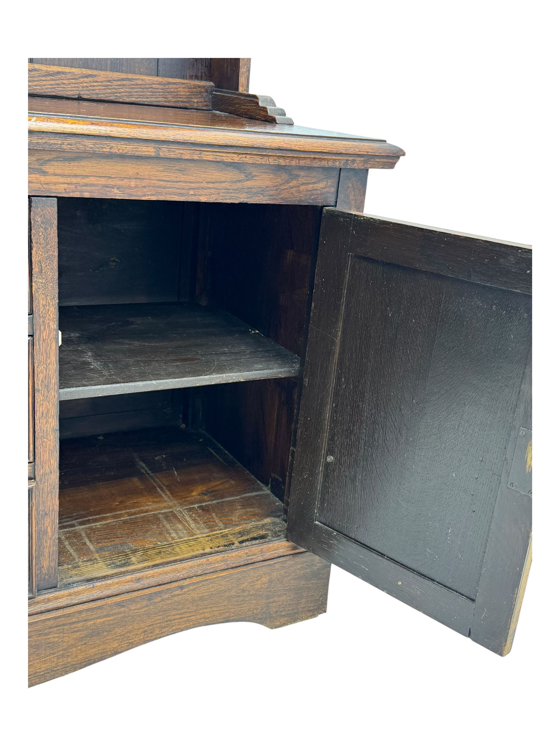Late 19th century oak dresser, the upper section with two shelves beneath a shaped cornice, the lower section with a central bank of three drawers flanked by cupboard doors, all decorated with geometric diamond motifs, the drawers fitted with brass handles, raised on a shaped plinth base
