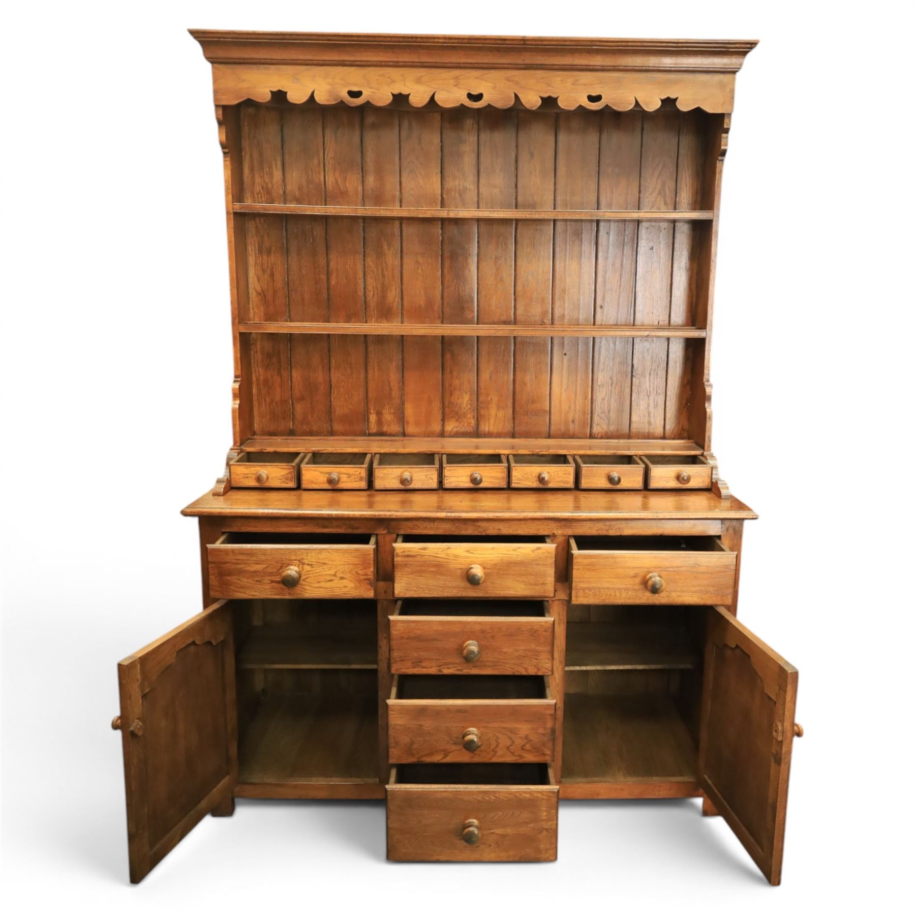 Traditional oak dresser with plate rack in the manner of Titchmarsh & Goodwin, plate rack with projecting cornice and shaped and pierced frieze, tongue and groove back three racks, over seven small spice drawers, the lower section with three short drawers, central bank three of drawers, fielded panelled sides and cupboard doors, raised on stile supports