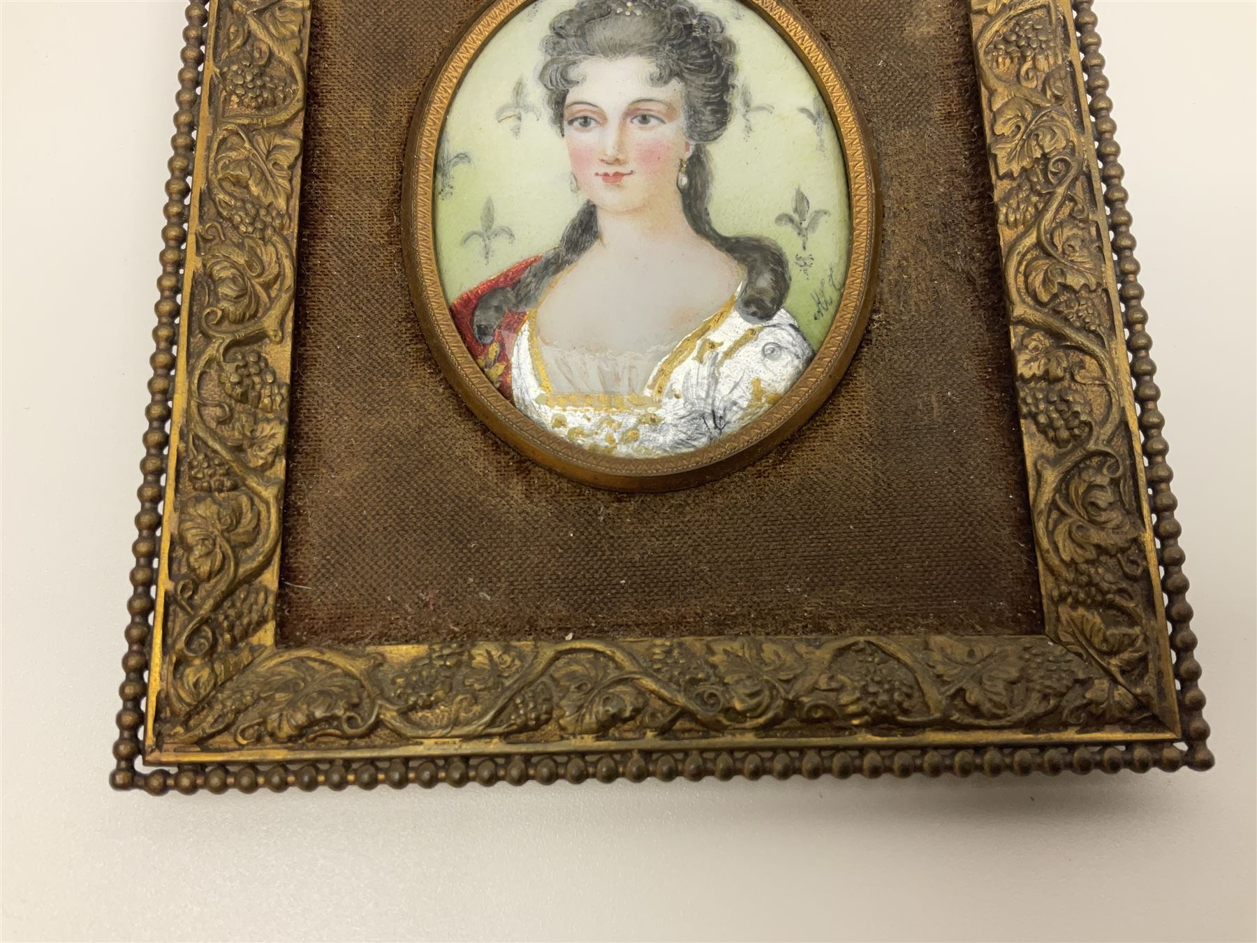 19th century portrait miniature on enamel, depicting a Georgian lady in period dress, hand painted with gilt detailing, in gilt frame with fruiting vine details, overall H13.7cm