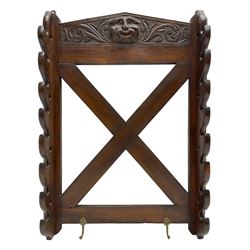 Victorian oak wall hanging whip or stick rack, sloped arch pediment carved with central grotesque mask with extended scrolling foliage, the upright supports cut with rests, x-framed back, two lower hooks