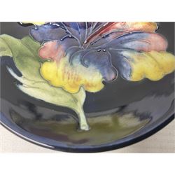 Moocroft small footed circular dish decorated in the Hibiscus pattern upon cobalt blue ground, with Queen Mary paper label beneath, together with a smaller example decorated in the Orchid pattern with impressed and printed W.Moorcroft marks beneath, largest, D9cm, (2)