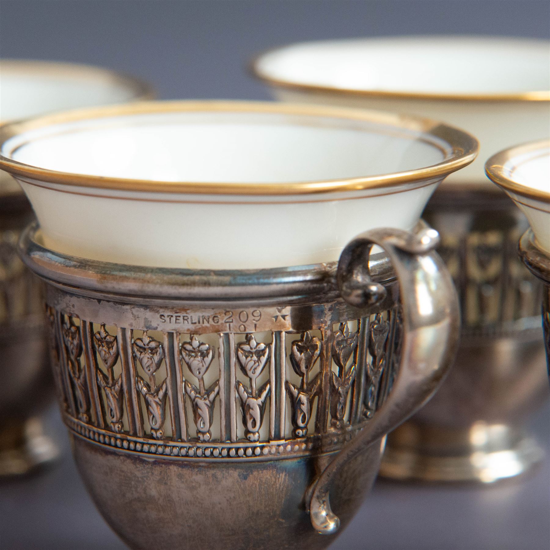 Set of six Lenox porcelain coffee cups, with gilt rims, each with American silver openwork cup holders, stamped sterling
