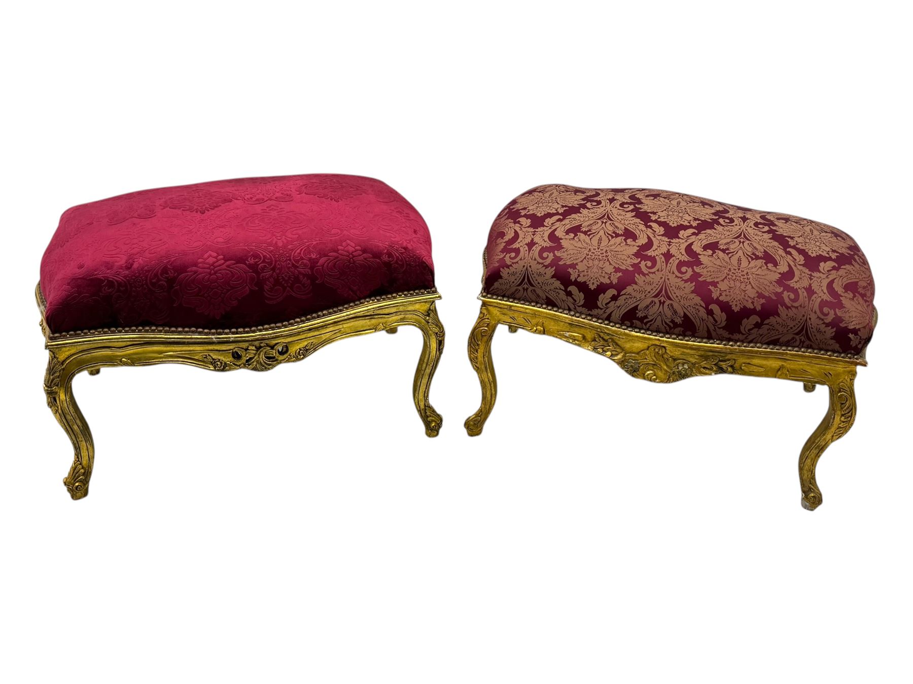 Pair of Louis XV-design giltwood stools, each upholstered in red damask fabric with slight variations in patterns, the carved frames adorned with scrolling foliage and shell motifs, raised on cabriole supports