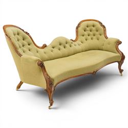 Victorian mahogany framed double ended chaise longue, serpentine button upholstered back with raised scrolled ends, padded arms and stuff-over seat upholstered in green fabric, carved showframe with foliate terminals and scroll supports, on short cabriole legs with brass castors