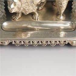 19th century Walker & Hall, silver plated inkstand, oblong and on four paw feet, the border decorated with pierced shell design, each side with a pen-rest, with two cut-glass bottles and central lion and urn finials, engraved to the front with an inscription, H15cm, L30cm