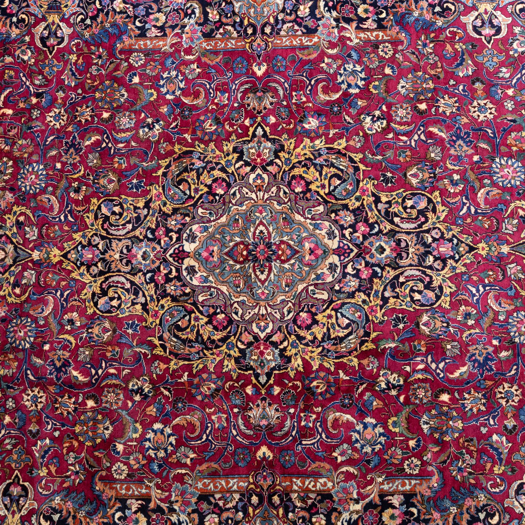 Large North East Persian Meshed hand-knotted carpet with signature, raspberry red field with central shaped cusped medallion, densely decorated with intricate arrangement of scrolling vines, and florals designs within conforming spandrels and a dark ground border richly ornamented with stylized flowers, vase and bird ornamentation, enclosed by guard stripes, with cotton fringe ends
