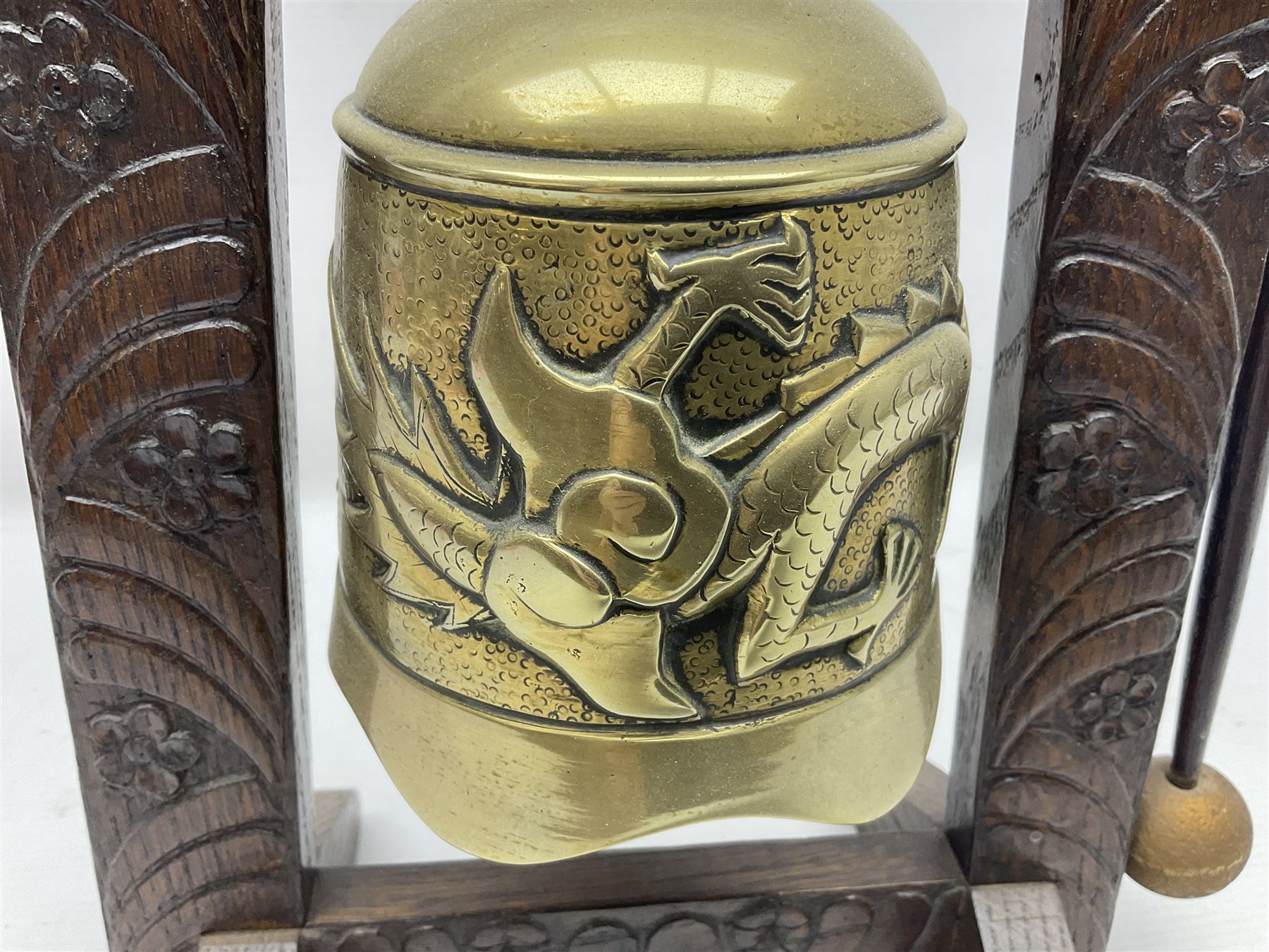 Chinese brass temple bell, decorated in high relief with a a dragon chasing a flaming pearl, within a carved floral hardwood stand, H36cm