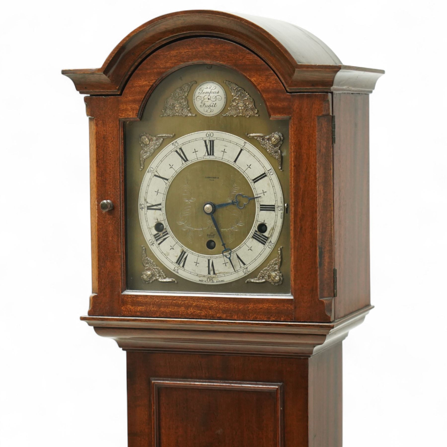 Carmichaels of Hull - mahogany cased 8-day musical grandmother clock c 1930 - with an arched pediment and arched hood, full-length trunk door on a short plinth raised on bracket feet, brass dial signed Tempus Fugit and Carmichaels of Hull with cast spandrels, matted dial centre and silvered chapter with Roman numerals, three train spring-driven movement chiming the quarters and hours on 8 gong rods with Westminster or Whittington chimes, movement stamped Elliott London with pendulum.