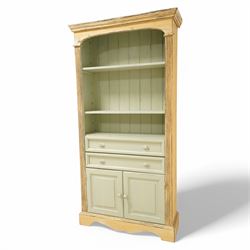 Painted open bookcase over two long drawers and cupboard, with arched cornice above two shelves, in a distressed yellow and sage green 