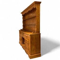 Late 20th century pine dresser, the plate rack with two fixed shelves and shaped apron over panelled back, base fitted with three drawers over two cupboard doors and central open niche flanked by turned uprights, on plinth base with shaped apron