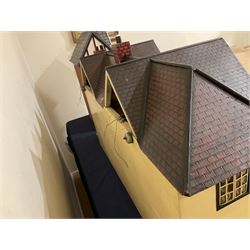 Large Tri-ang No.93 doll`s house in the 'Stockbroker's Range' c1935; two-storey double-fronted Tudor design, half timbered gables, two-storey bay windows, cream and mock shrubbery to front, opening metal framed windows with green shutters, red simulated tiled roof with chimney, integral garage with opening doors, front elevation has four hinged doors opening to reveal two bedrooms with fire places, living room, bathroom and kitchen with built in dresser and sink, entrance hall and staircase, side entrance with porch and seat and sun dial over on chimney stack; some wiring for electrical lighting; metal Tri-ang Toys disc verso; comprehensively furnished H66cm L117cm D43cm