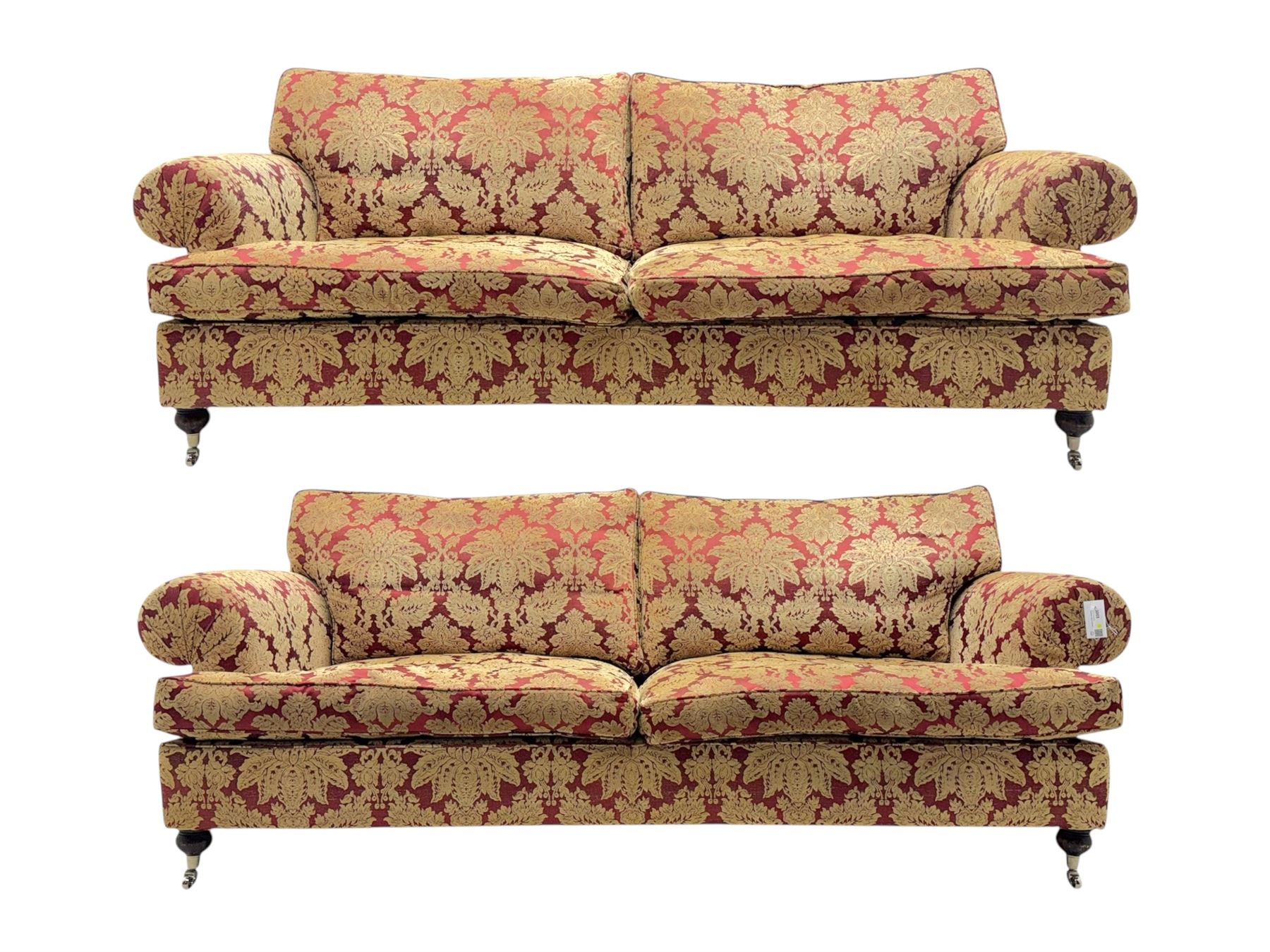 Duresta - pair of Grande three-seat sofas, traditional shaped with rolled arms and upholstered loose cushions, in red ground fabric with raised gold foliate pattern, on turned feet with brass castors 
