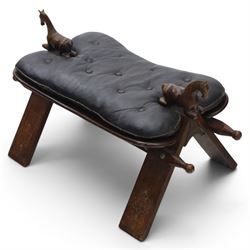 20th century saddle stool, wiht black leather seat, surmounted with carved horses, on an X-frame base with brass inlay
