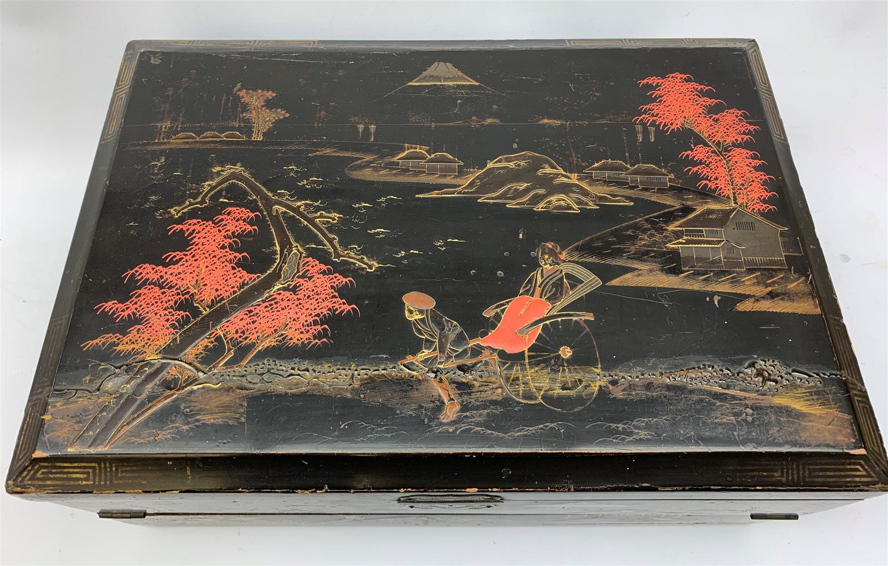  A 20th century Chinese black lacquer and gilt detailed writing box, decorated with figures, pagodas and cranes amidst a mountainous landscape, the hinged cover opening to reveal a compartmented interior and fold out baize lined slope, H20cm L46.5cm D31.5cm.   