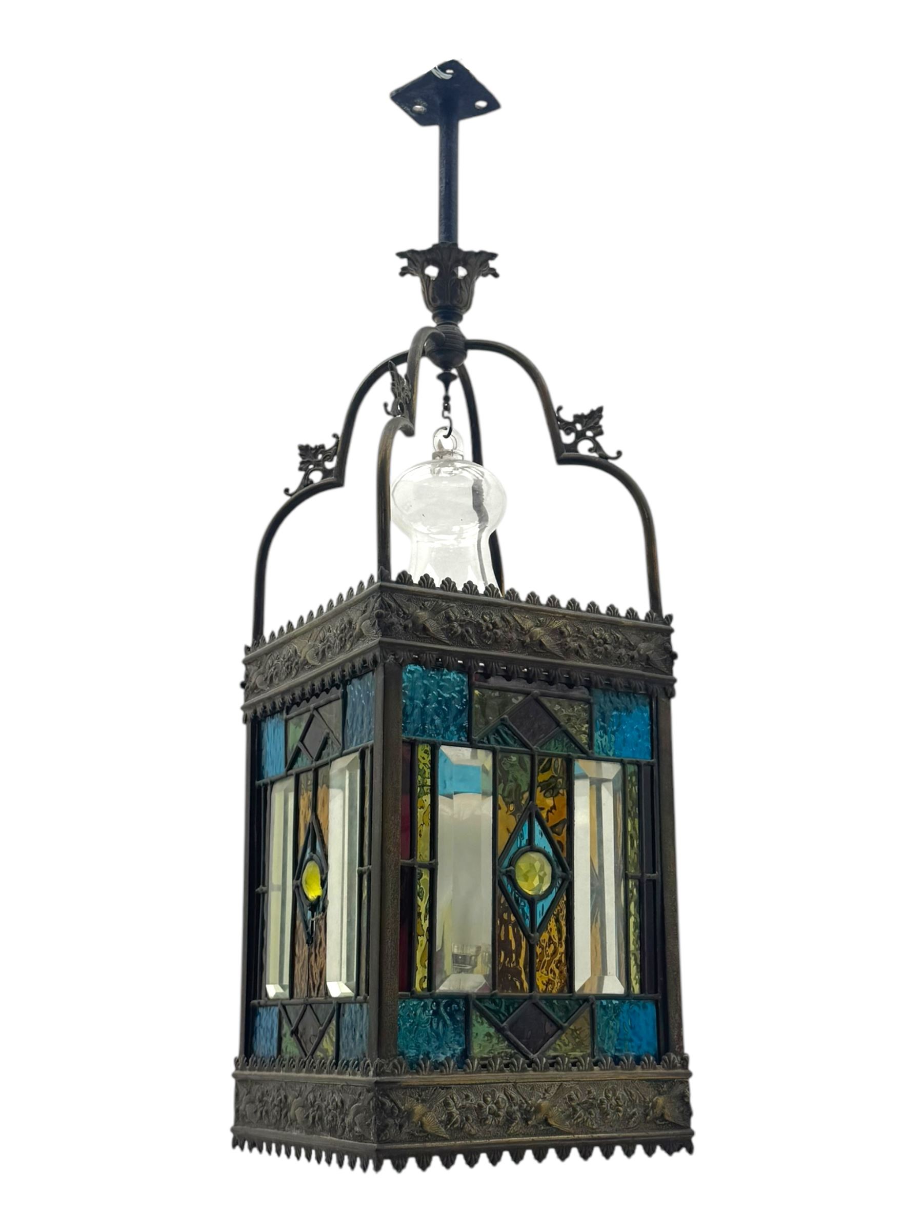 20th century Gothic design stained glass and brass hall lantern, with ornately decorated frieze and apron, with geometric coloured glass panels and eight rectangular bevelled glass panels, with bell shade, wired for electricity 