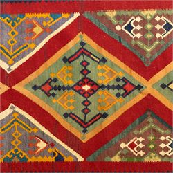South West Persian Qashqai flatweave kilim, madder red ground with stacked diamond panels filled with latch hook and angular floral motifs, enclosed by multiple geometric borders in palettes of indigo, green, and ochre 