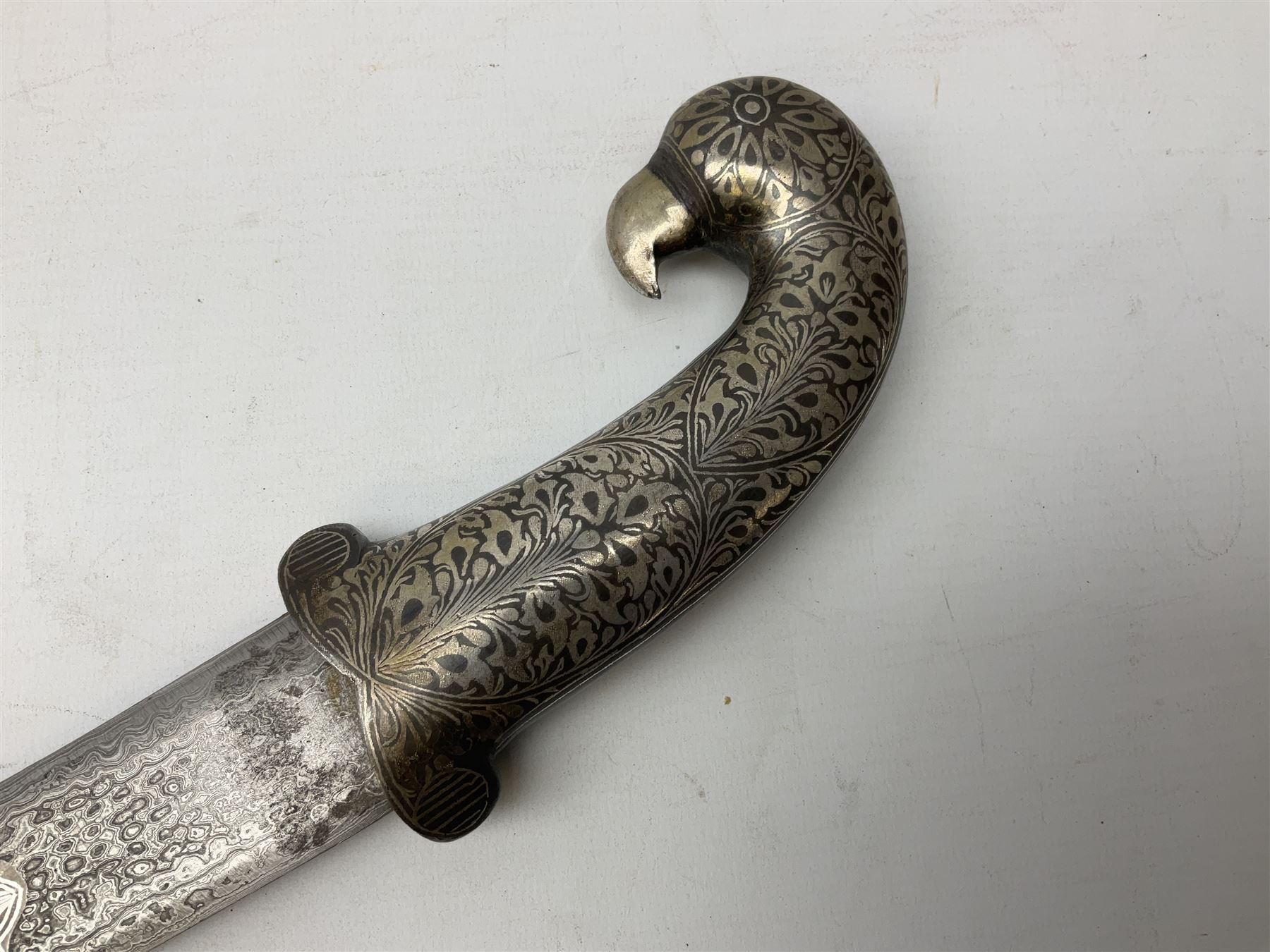 Indian Khanjar dagger with 28cm curving damascus steel blade inlaid with silver floral emblem, white metal and niello style grip in the form of a bird's head with pronounced beak and matching scabbard L44cm overall