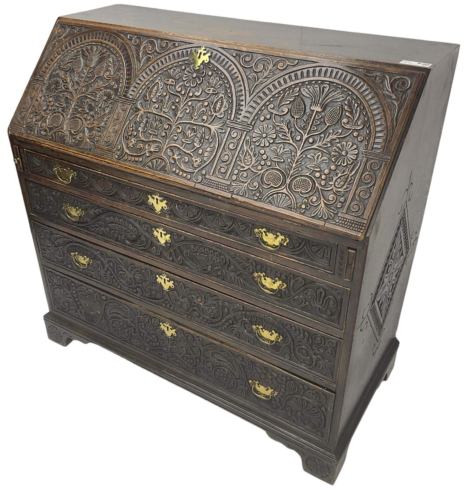 18th century heavily carved oak bureau, the fall front relief carved with three arches enclosing plants and flower head decoration, the interior fitted with pigeonholes, drawers and cupboard, four graduating cock-beaded drawers below, carved with lunettes and trailing foliage decoration, on bracket feet