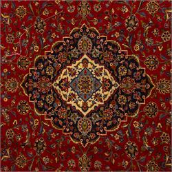 Central Persian Kashan hand-knotted carpet, crimson ground, with a central shaped palmette medallion with pendants, surrounded by scrolling foliate and floral motifs incorporating rosettes, palmettes, and vine work, enclosed by a dark navy with repeating border with repeating palmettes and meandering vines, flanked by floral guard stripes, with cotton fringes 